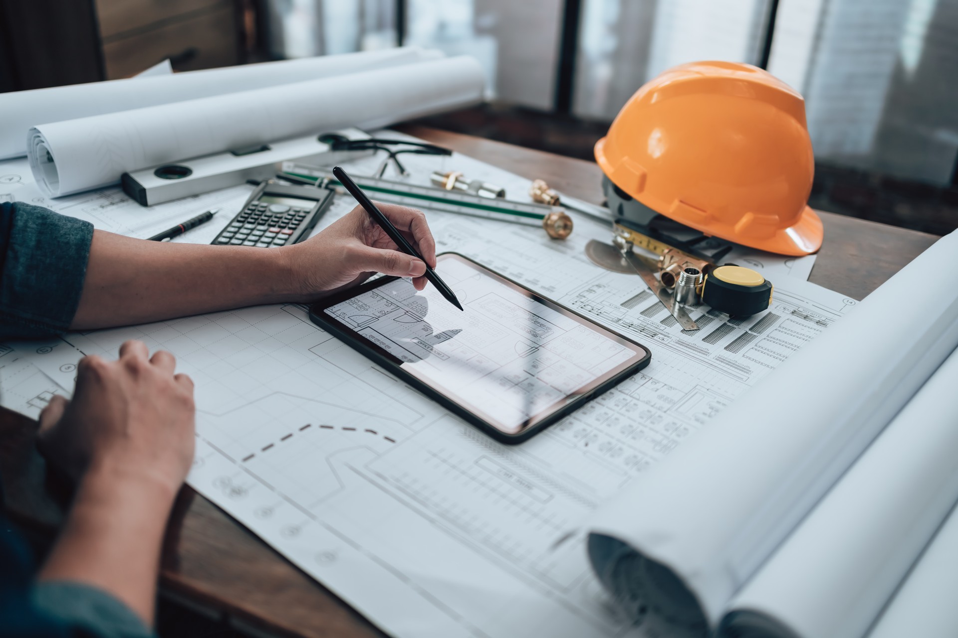 Engineering working with drawings inspection on tablet in the office and Calculator, triangle ruler, safety glasses, compass, verniear caliper on Blueprint. Engineer, Architect, Industy and factory concept.